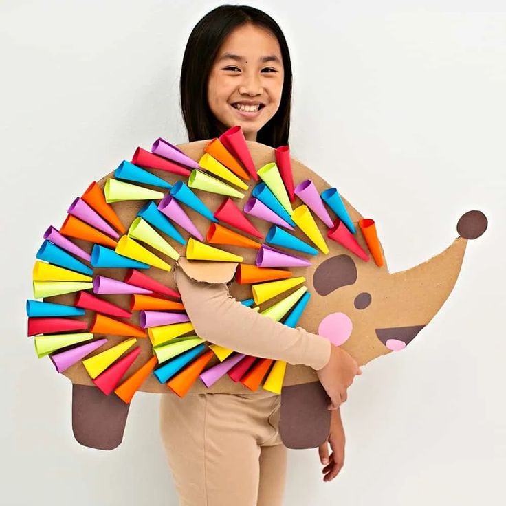 a woman is holding a cardboard hedgehog with colored strips on it's body