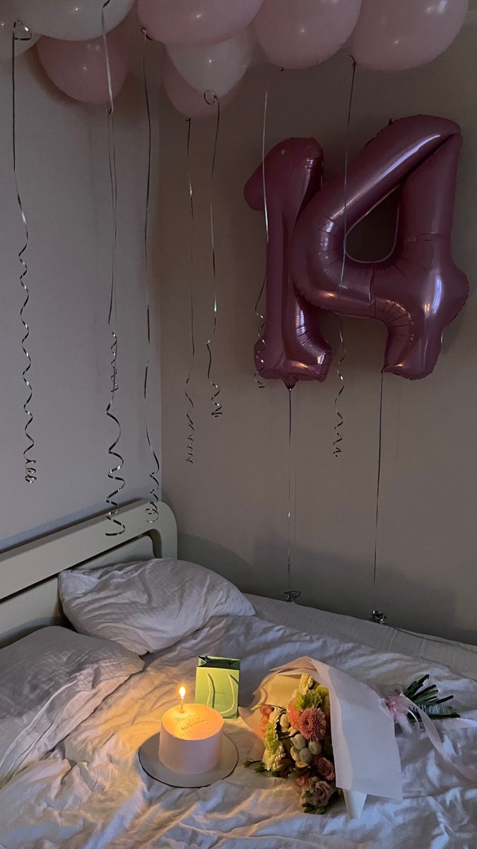 a birthday cake on a bed with balloons in the background and a lit candle next to it