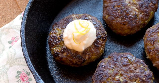 four hamburger patties in a cast iron skillet with mayonnaise on top