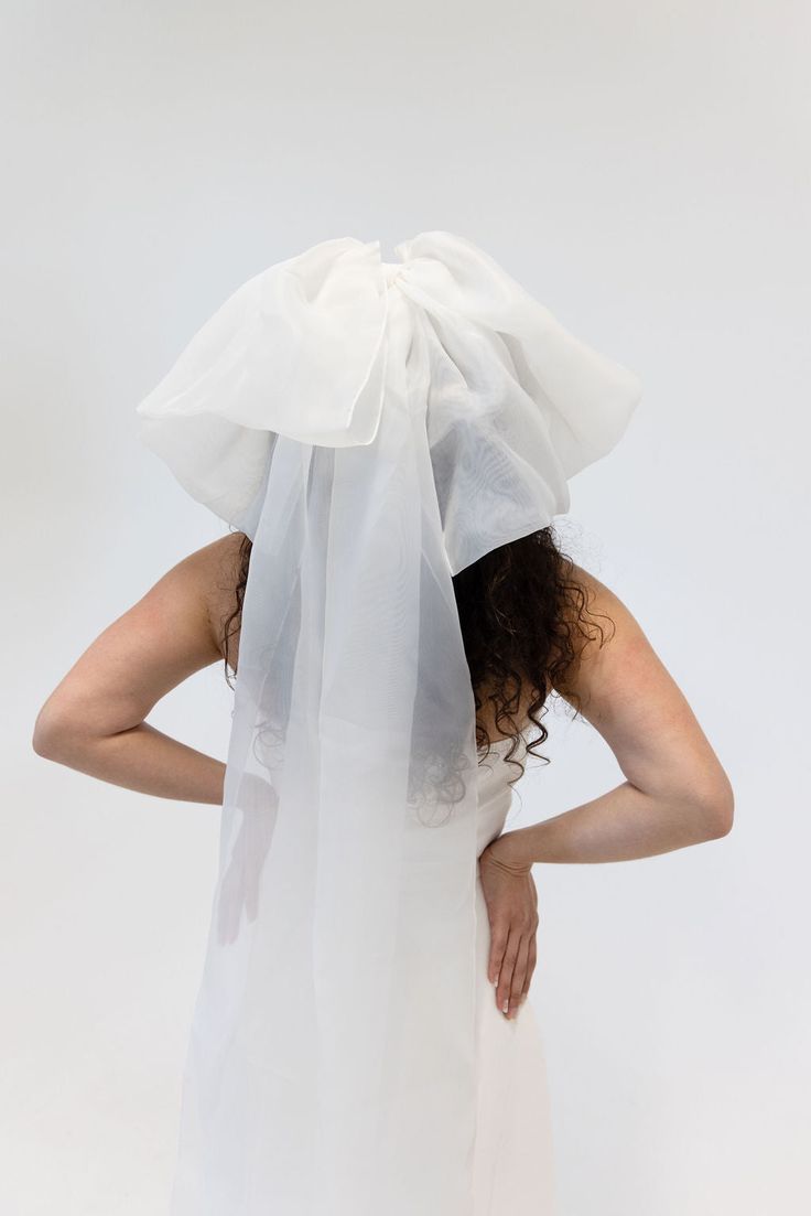 a woman in a white dress with a veil on her head and hands behind her back