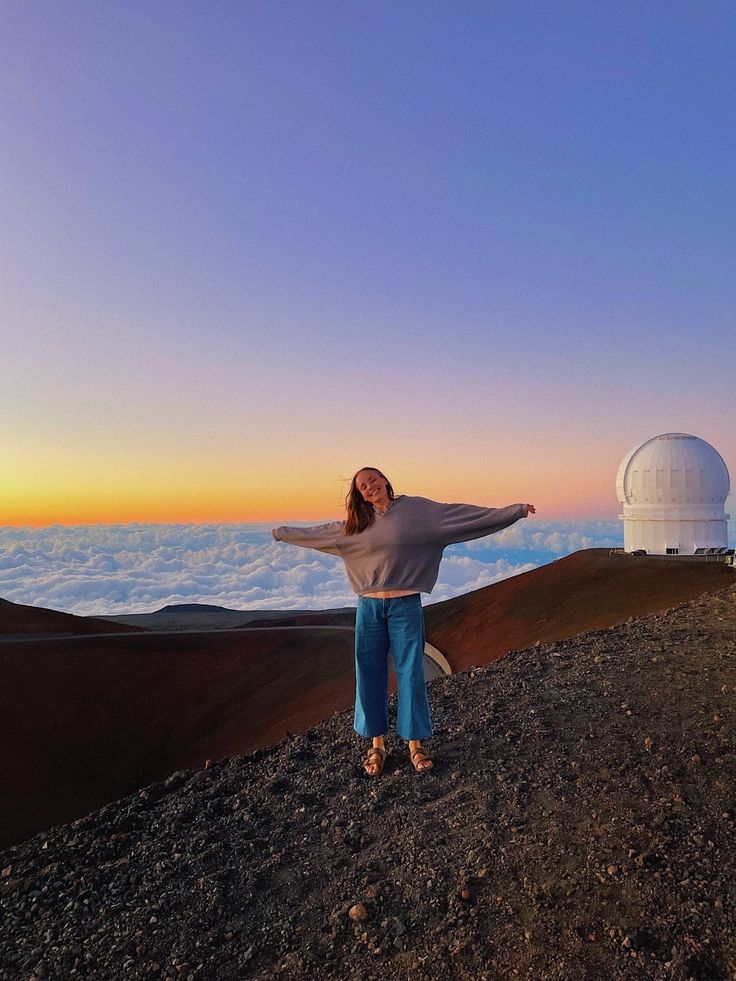 a woman standing on top of a mountain with her arms outstretched