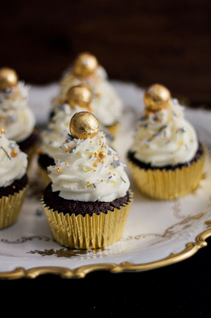 cupcakes with white frosting and gold decorations on a platter, ready to be eaten