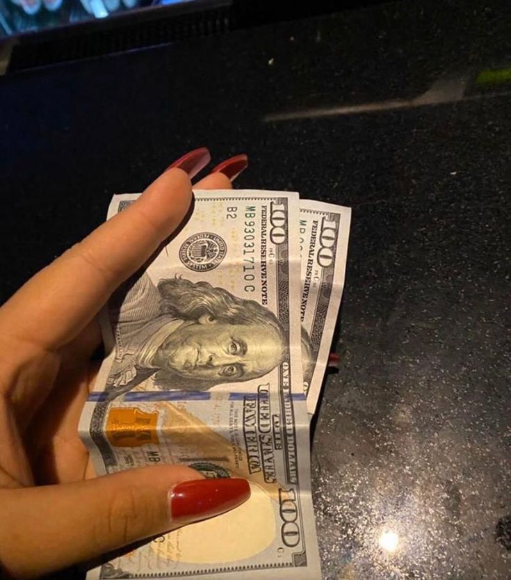 a woman's hand holding money on top of a counter