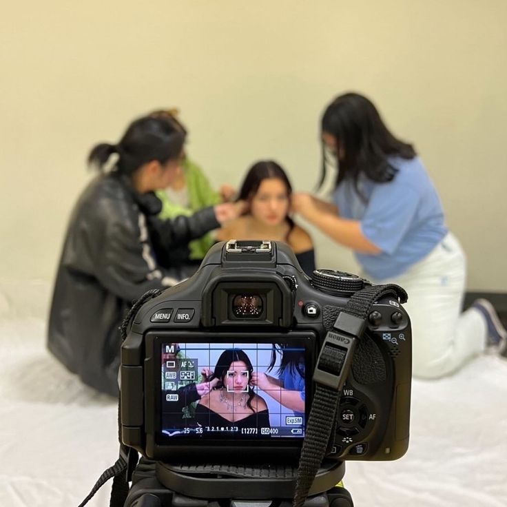 two women are sitting on the bed and one is taking a photo with her camera