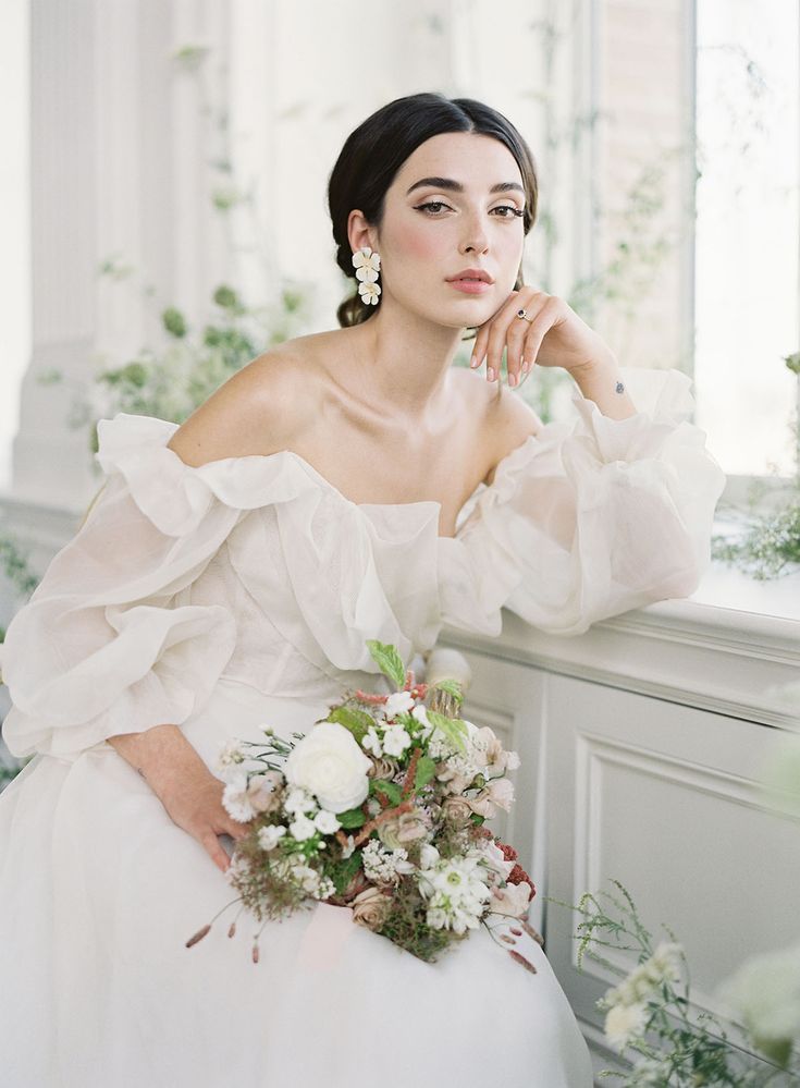 a woman in a white wedding dress sitting on a window sill with flowers and greenery