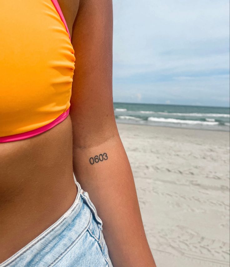 a woman with a small tattoo on her left arm standing in front of the ocean