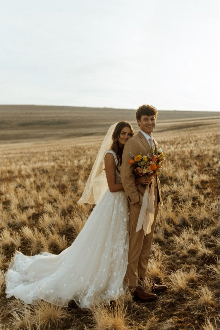 a bride and groom standing in the middle of an open field with tall dry grass