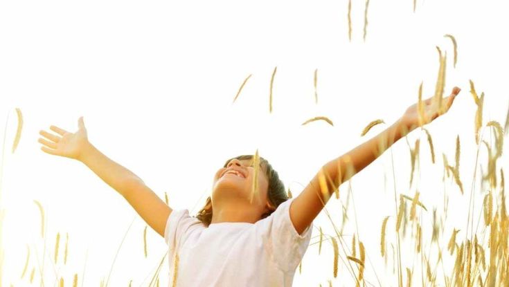 a woman standing in tall grass with her arms spread out to catch the sun's rays