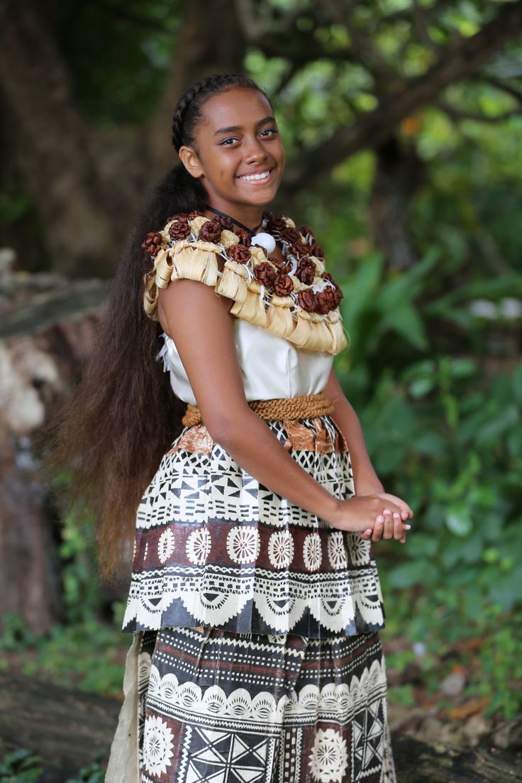 a woman wearing a skirt and smiling at the camera with trees in the back ground behind her