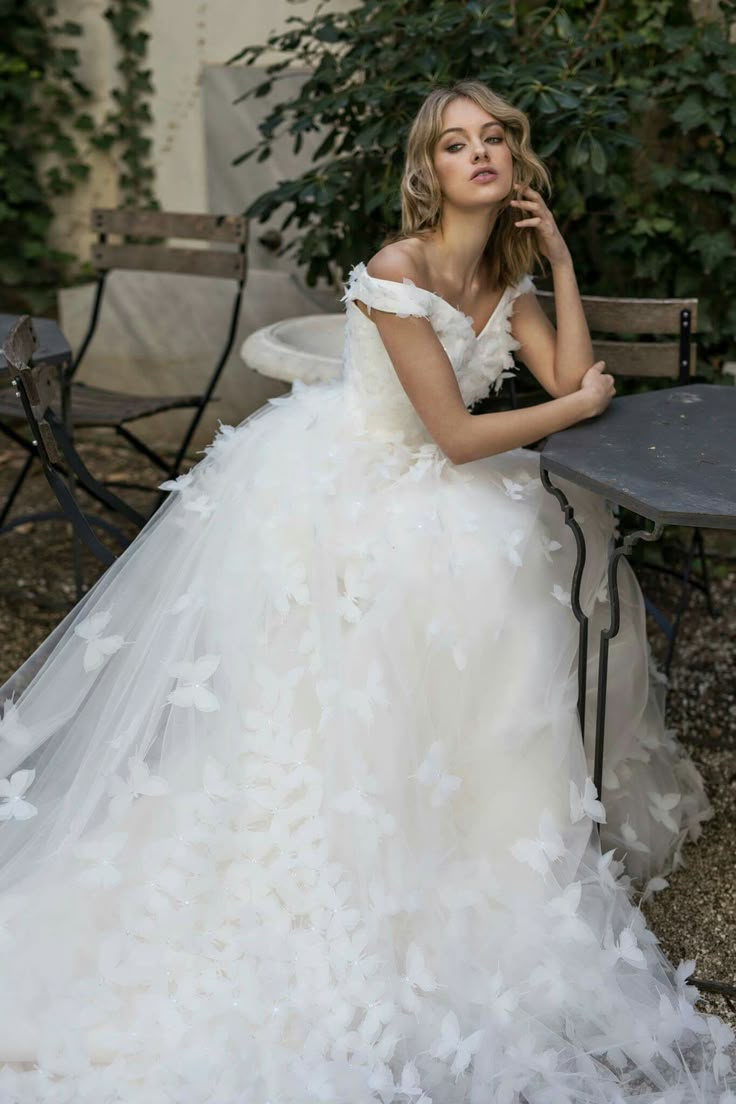 a woman in a wedding dress sitting at a table with her hand on her chin