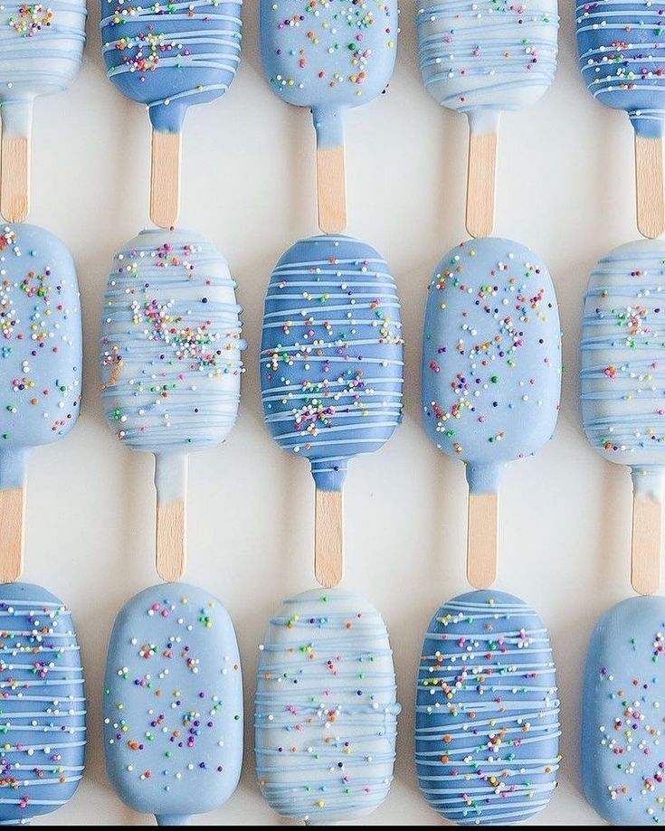 blue cake pops with sprinkles are arranged in rows on a white surface