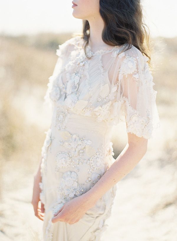 a woman standing in the sand wearing a dress with flowers on it's shoulders