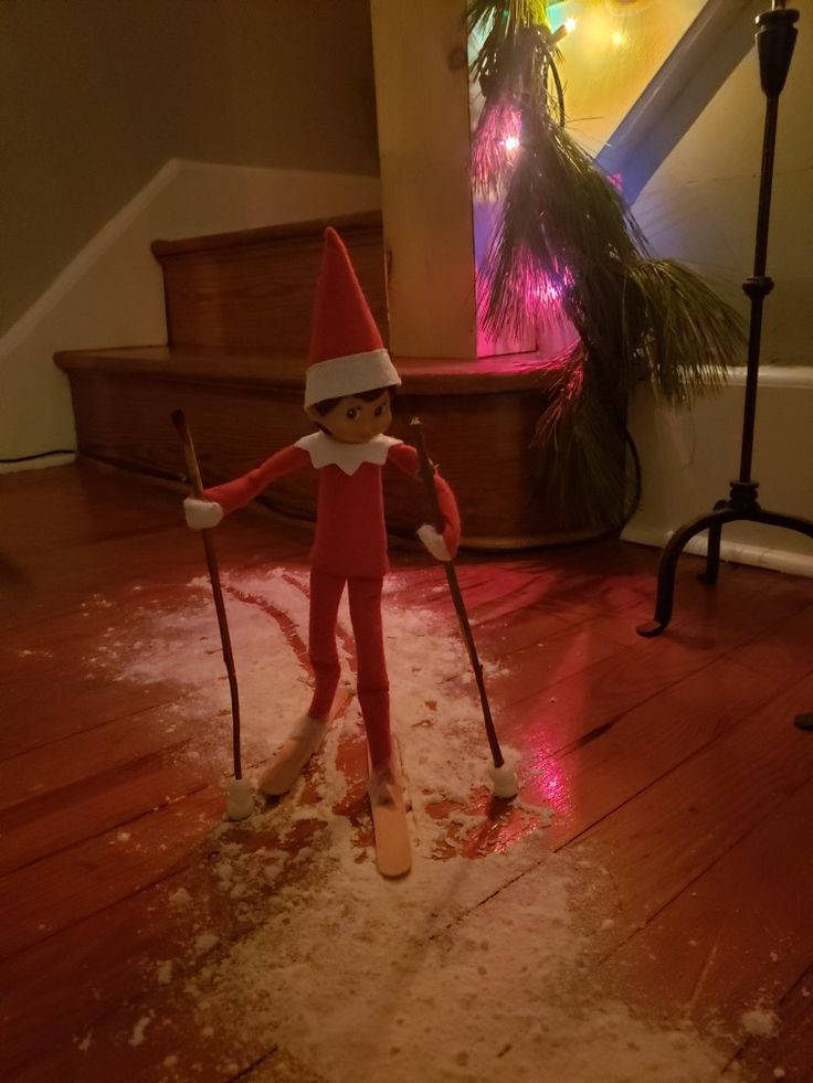 an elf with skis and poles standing on the floor in front of a christmas tree