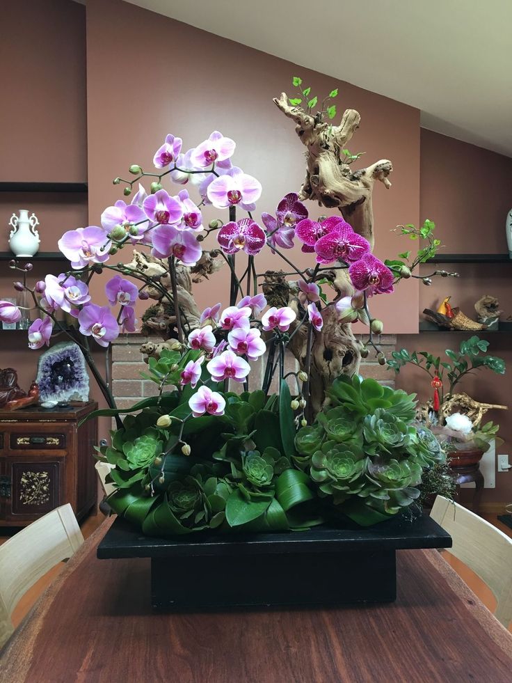 purple flowers are in a black vase on a table with green leaves and other plants