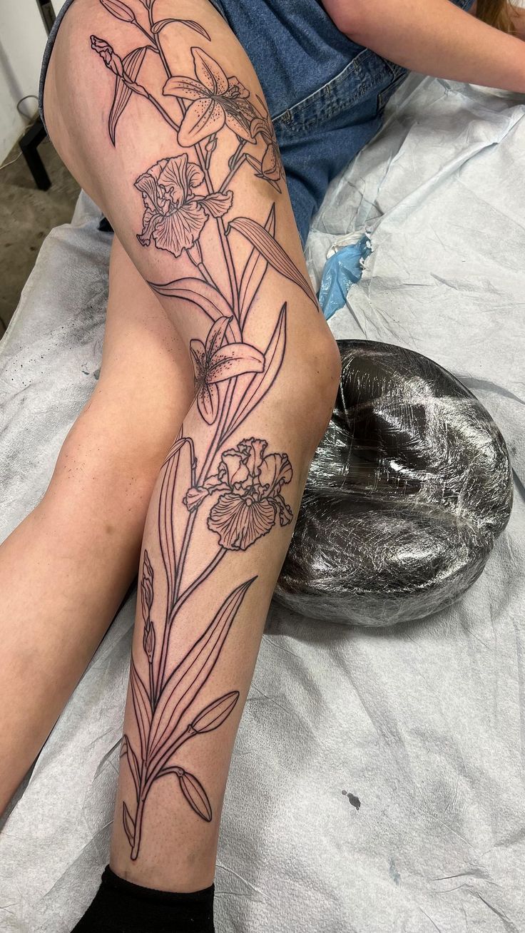 a woman sitting on top of a bed with her legs crossed and flowers tattooed on the leg