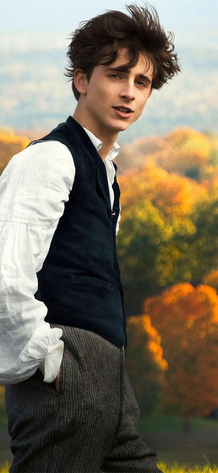 a young man in a vest and tie posing for a photo with trees in the background