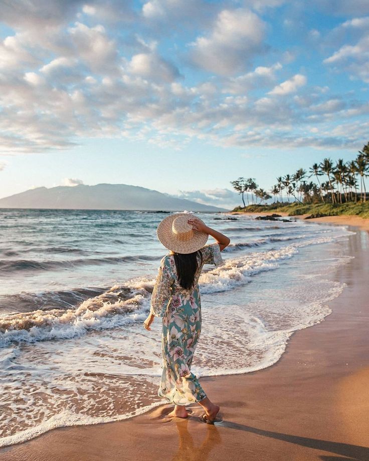 a woman walking along the beach with a straw hat on her head and palm trees in the background