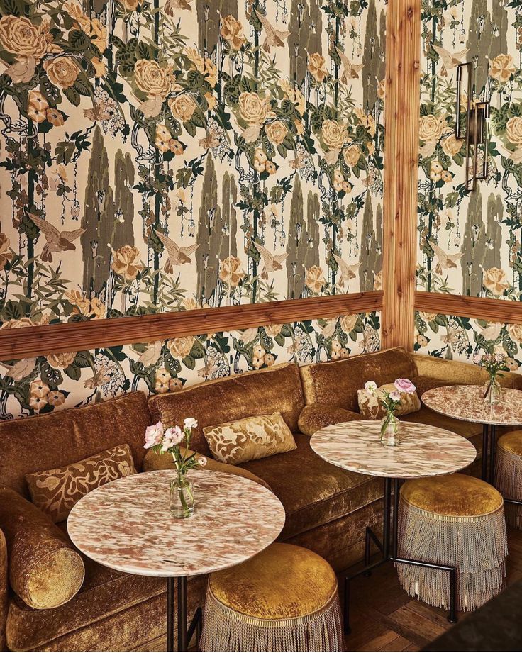 an ornately decorated restaurant with floral wallpaper and gold velvet boothes, round tables and stools