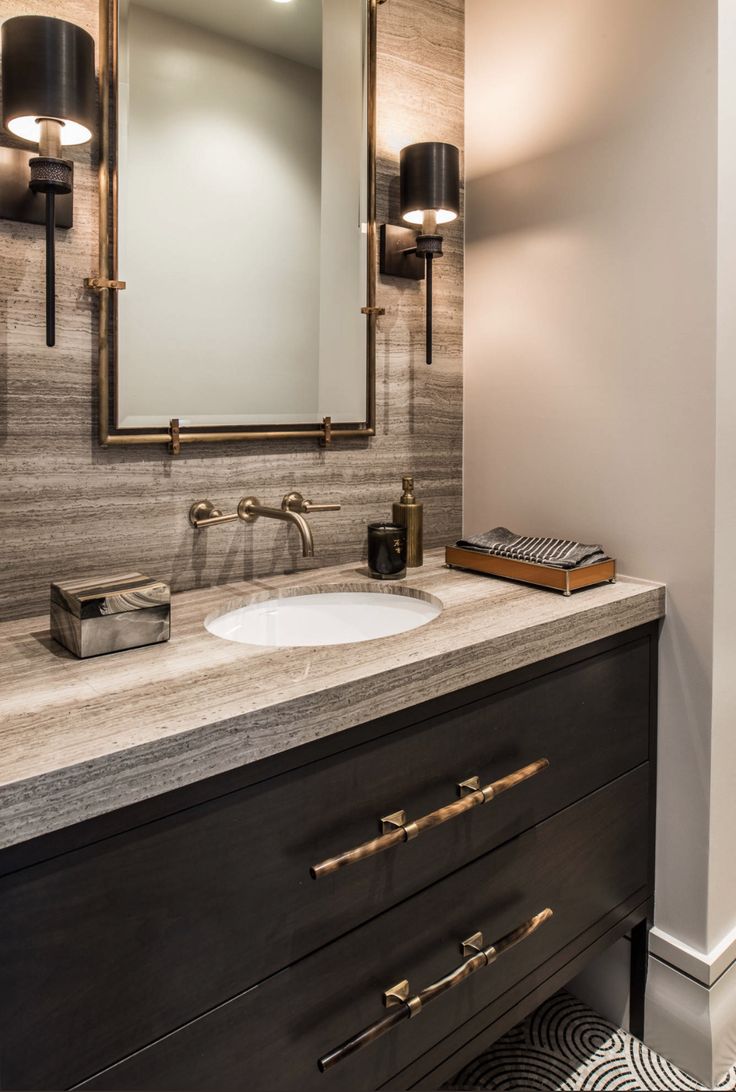 a bathroom vanity with marble counter top and gold accents on the mirror, along with two lights