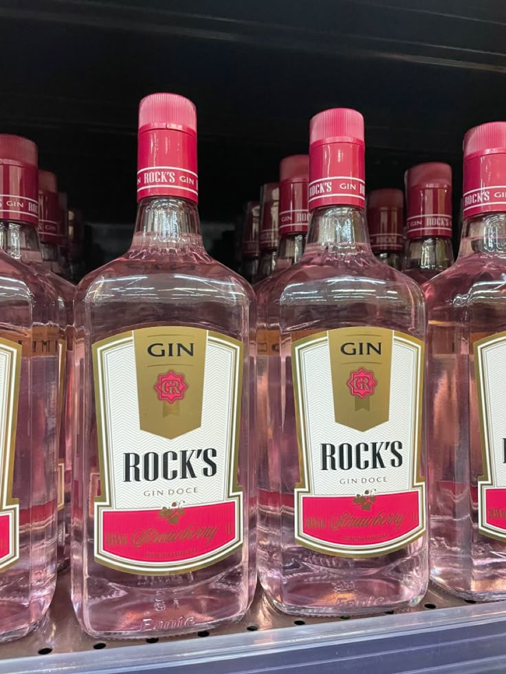 bottles of gin are on display for sale in a grocery store, with one being red and the other is pink