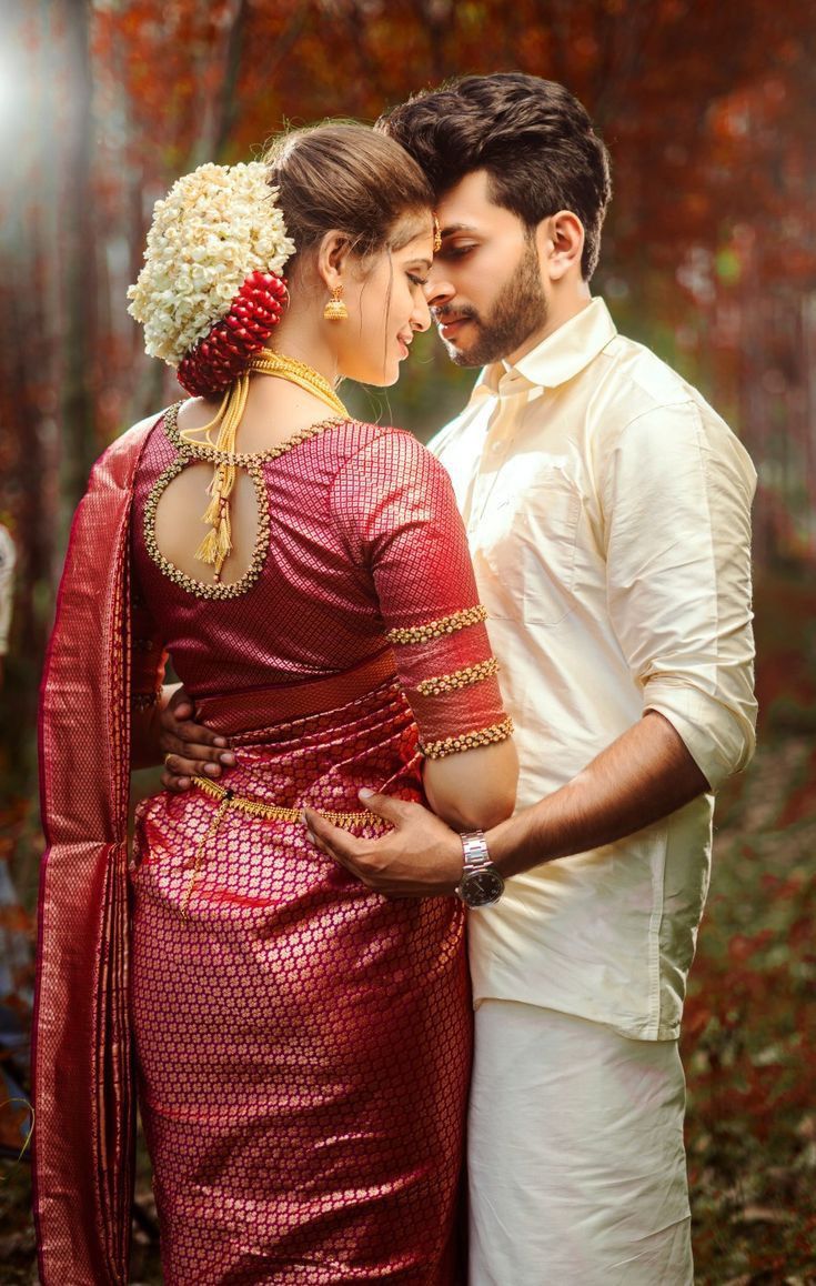 a man and woman standing next to each other in front of trees with leaves on the ground