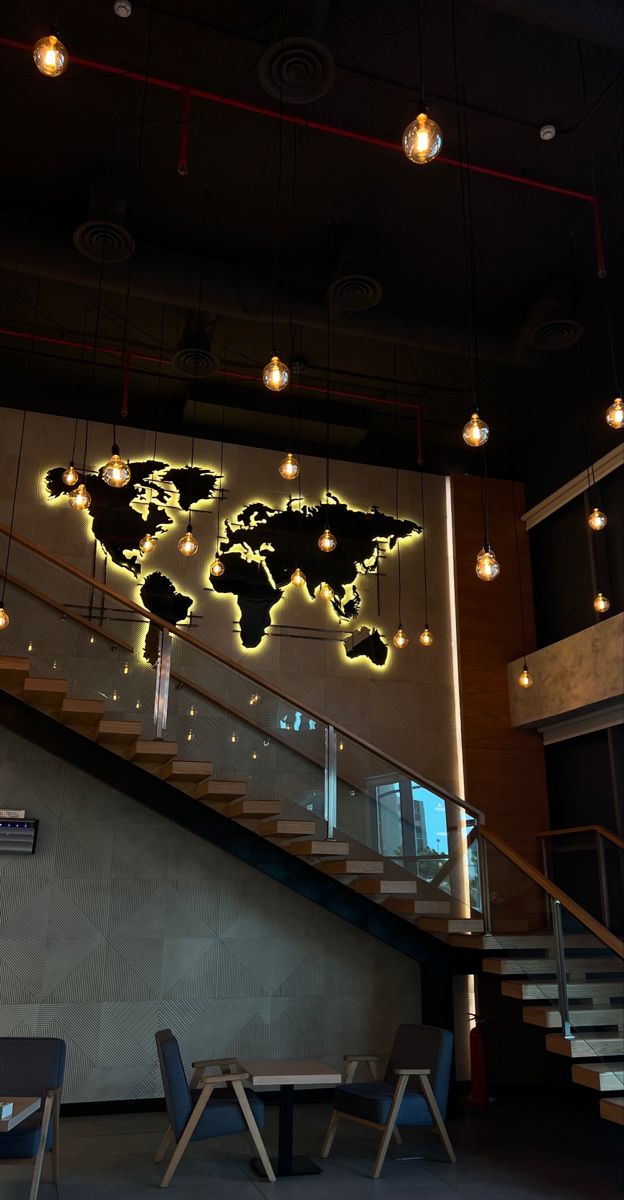 a world map on the wall next to some tables and chairs in a room with stairs