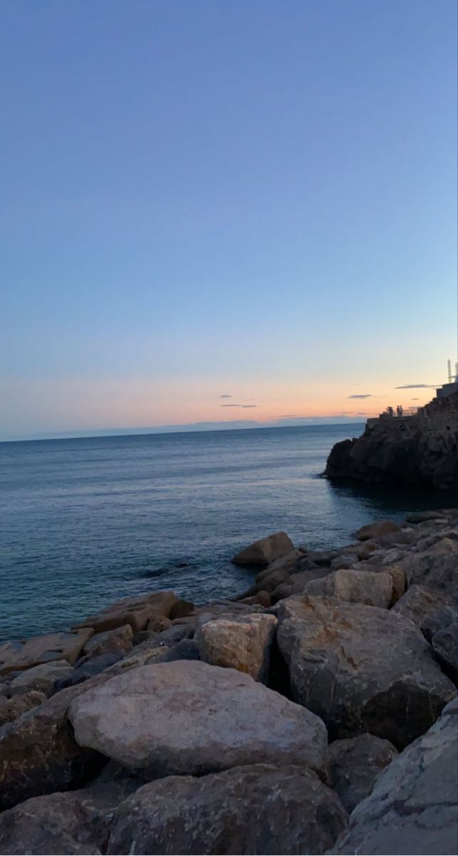 there is a bench sitting on the rocks by the water's edge at sunset