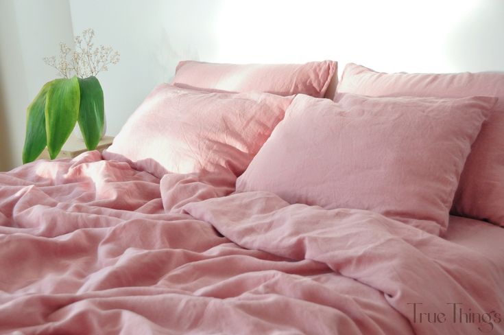 a bed with pink sheets and pillows on top of it, next to a potted plant