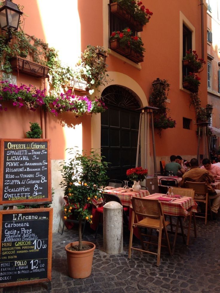 an outdoor cafe with tables and chairs in front of the building that has flowers growing on it