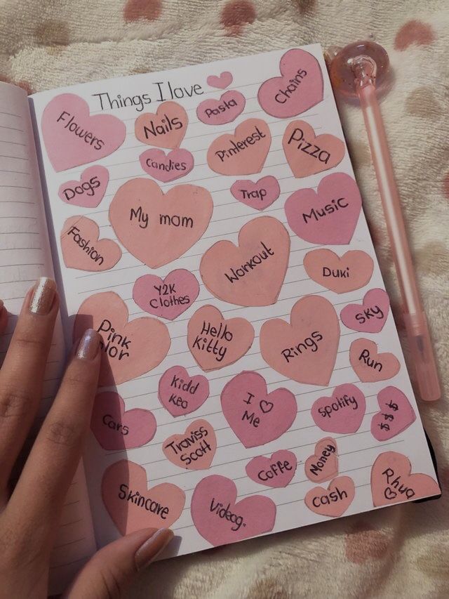 someone is writing on a notebook with pink hearts and words written in the pages that spell out things i love