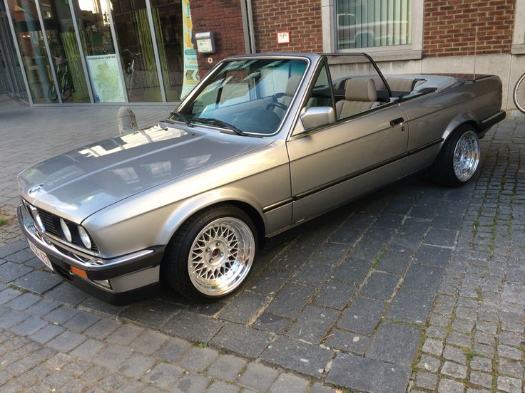 a silver convertible car parked on the side of a street next to a brick building