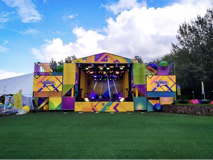 an outdoor stage set up with bright colors and decorations on the grass at a festival