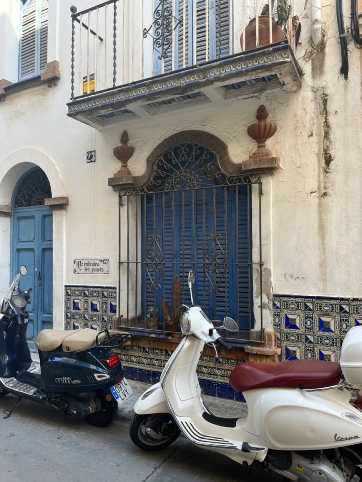 two mopeds are parked in front of a building with blue doors and windows