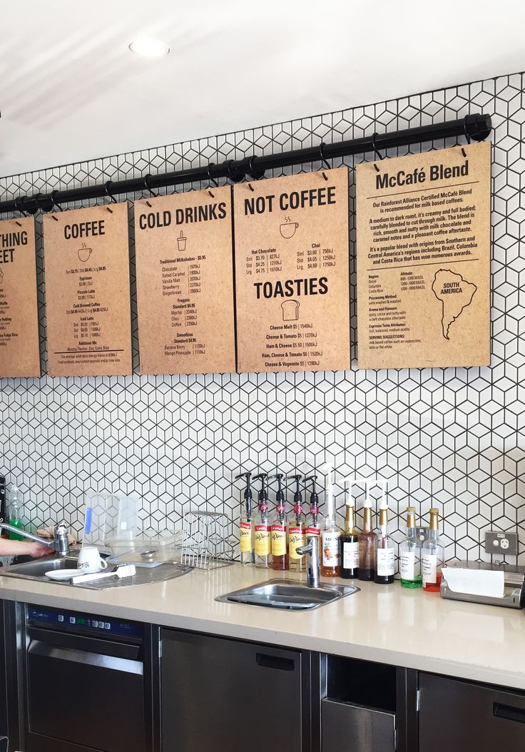 a woman standing in front of a counter filled with drinks and coffee cups, next to two menus on the wall