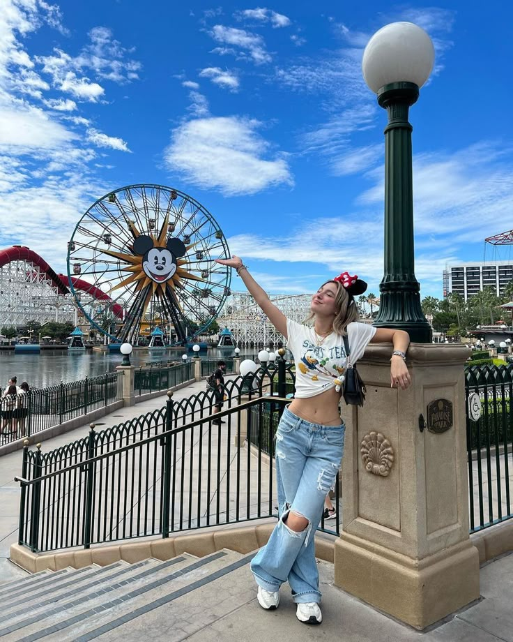 a woman standing next to a light pole near a fence and roller coasters in the background