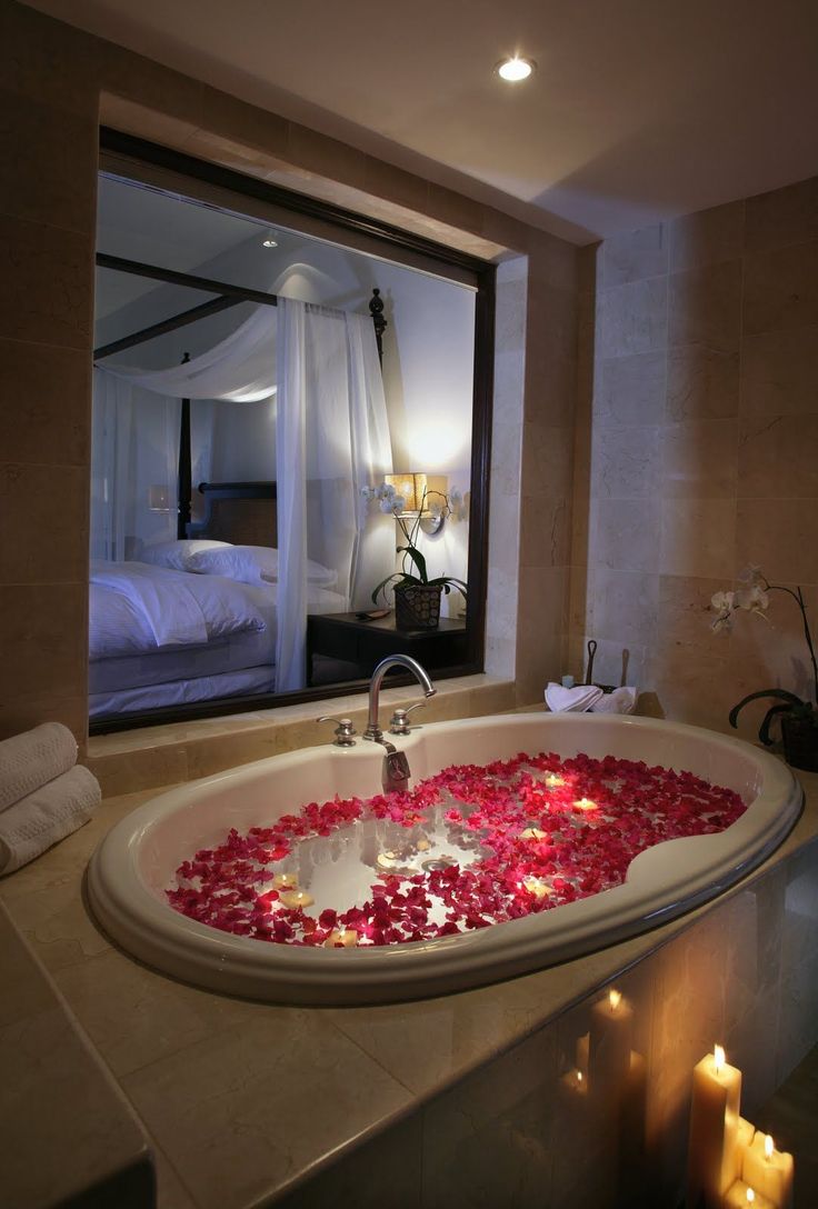 a bathtub filled with rose petals in front of a large mirror and lit candles