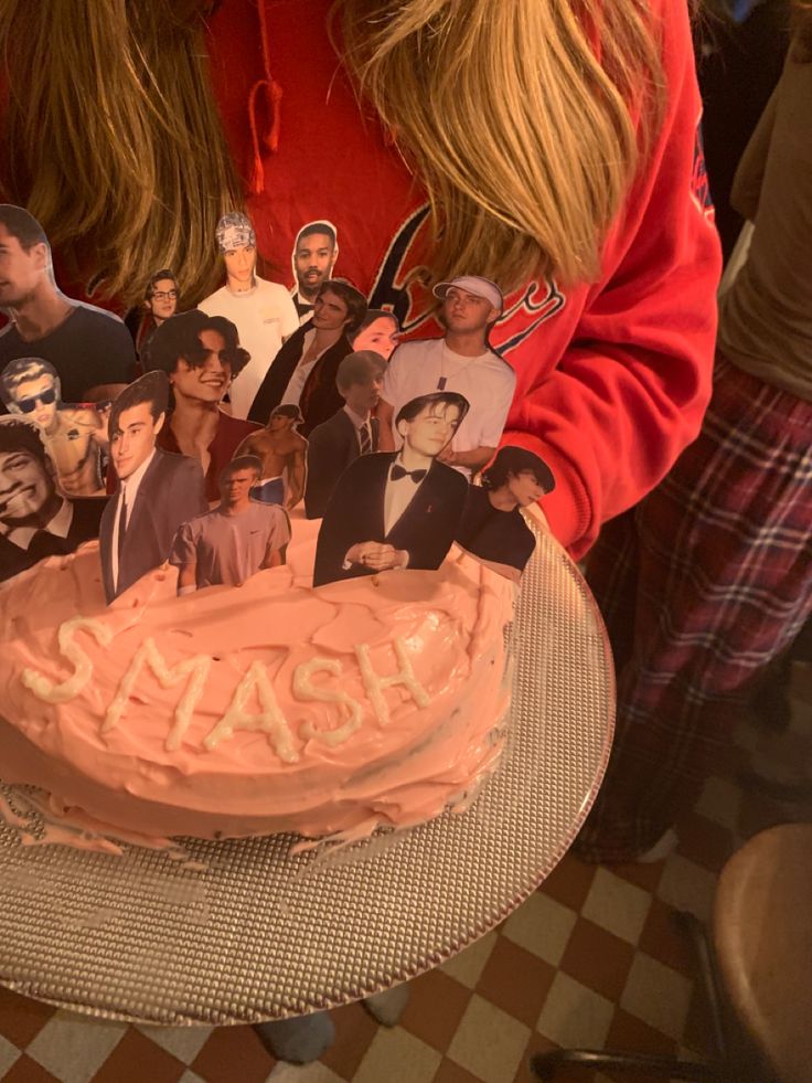 a woman holding a cake with pictures of people on it and the words smash spelled in frosting