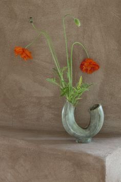 three orange flowers in a green vase sitting on some concrete steps with no one around them