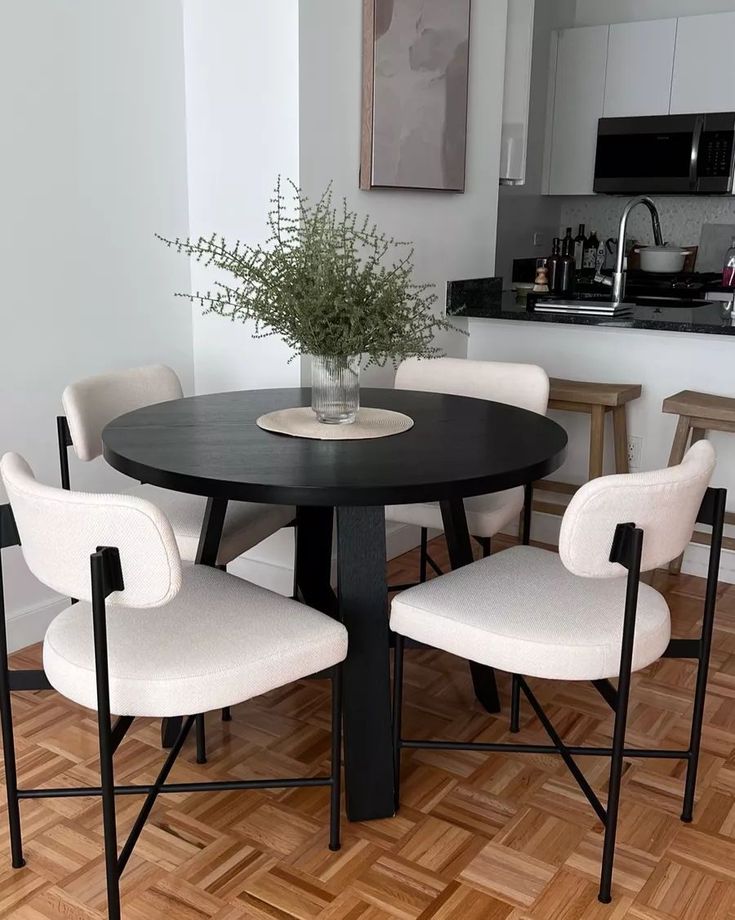 a black table with four white chairs around it and a potted plant in the center