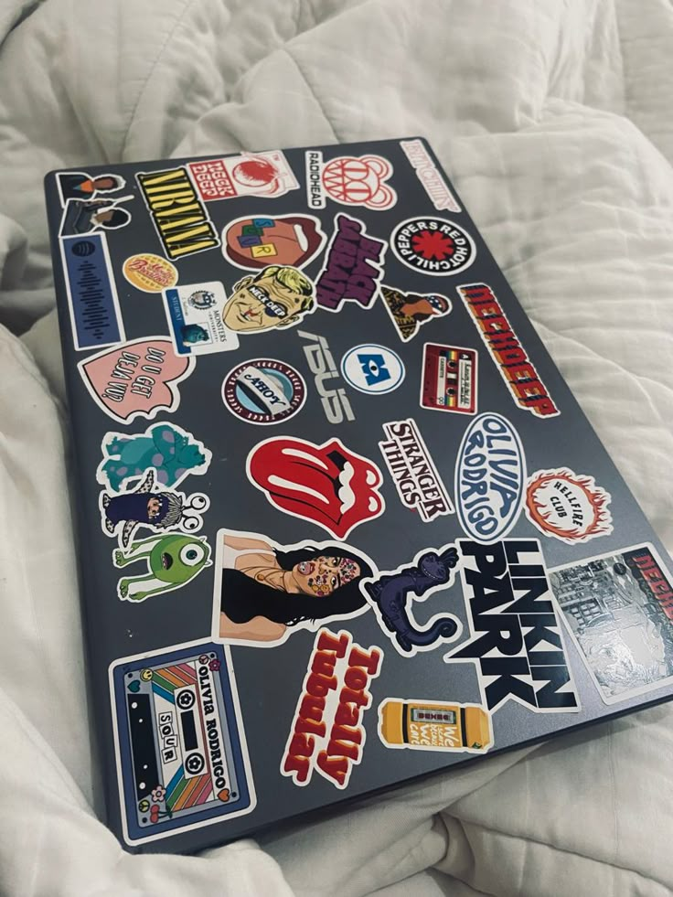 a laptop covered in stickers sitting on top of a bed