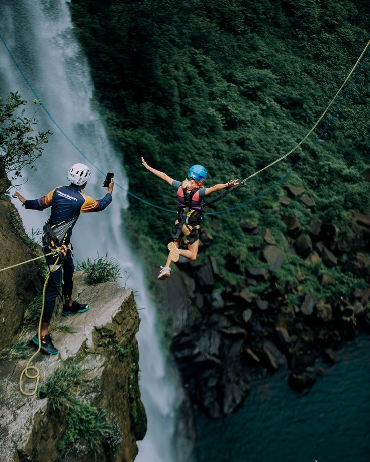 two people are rapping in front of a waterfall while another person is holding onto the rope