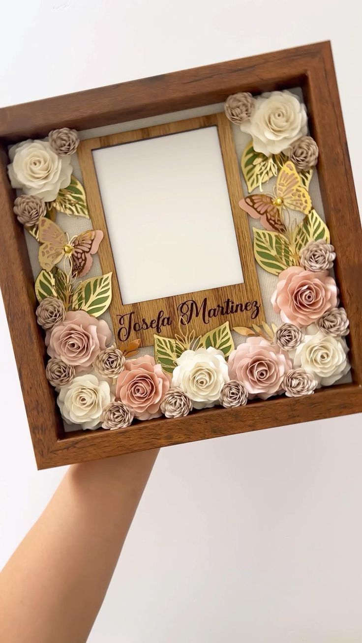 a person holding up a wooden frame with flowers on it