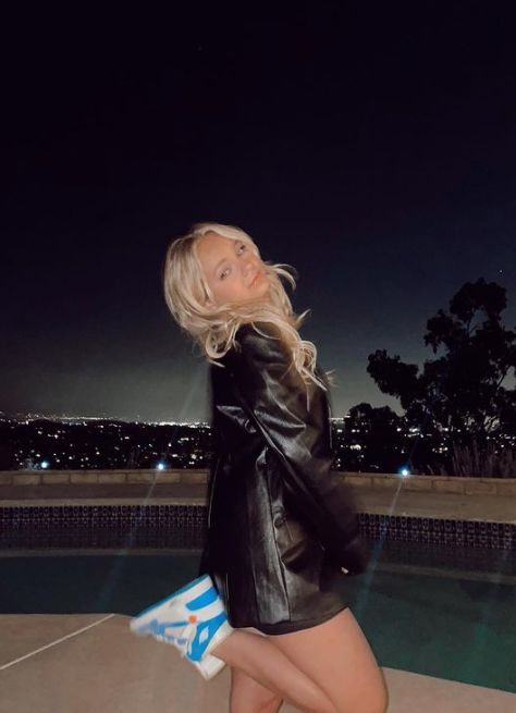 a woman in black jacket and shorts standing next to a pool