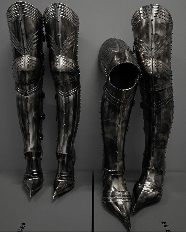 two metal boots are on display in front of a gray wall and another pair is behind them