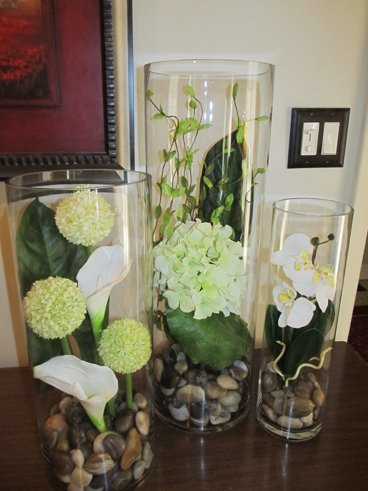 three glass vases with flowers and rocks in them