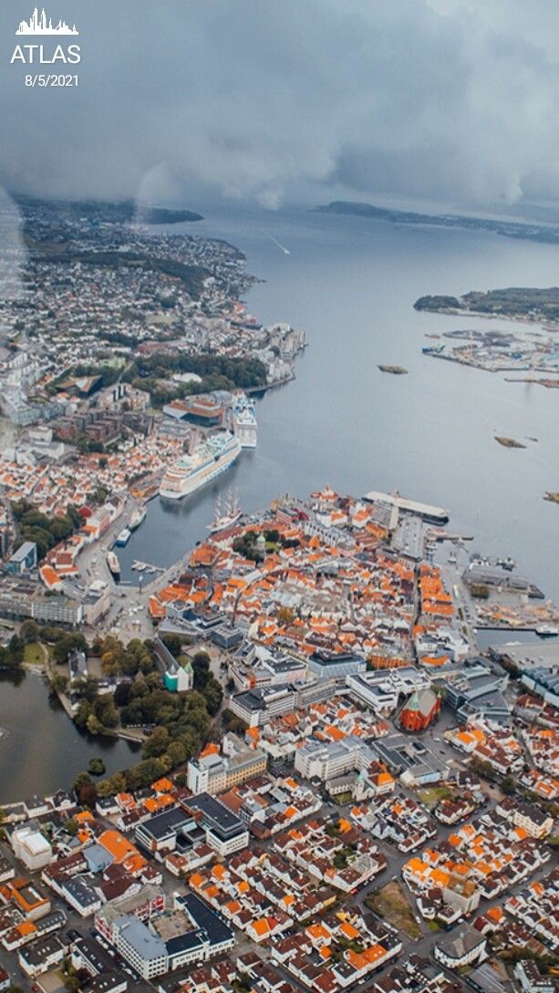 an aerial view of a city with orange roofs and water in the foreground, on a cloudy day