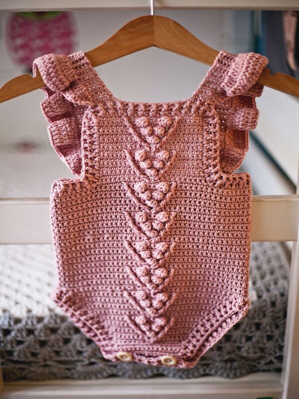 a pink crocheted bodysuit hanging on a wooden hanger