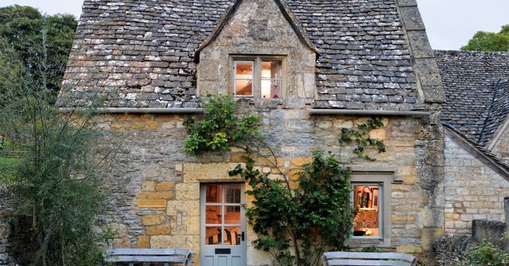 an old stone house with ivy growing on it's roof and two wooden benches in front