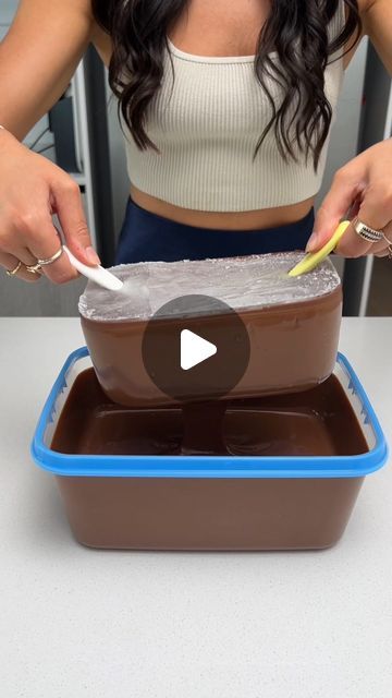 a woman cutting into a chocolate cake in a plastic container with two yellow handled utensils