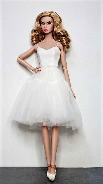 a barbie doll wearing a white tulle dress and high heeled shoes is posed in front of a wall